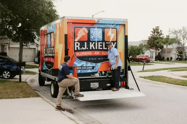 Two RJ Kielty technicians preparing to unload equipment from a large branded service truck parked on a residential street for a home service call